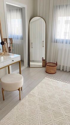 a room with a white rug, mirror and dressing table in front of the window