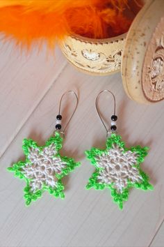 two green and white crocheted earrings sitting on top of a wooden table next to an orange feather