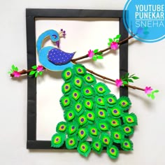 a paper peacock sitting on top of a tree branch in front of a framed photo