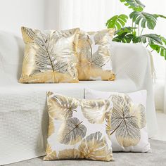 three decorative pillows on a couch next to a potted plant