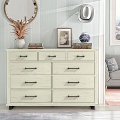 a white dresser sitting in a living room next to a gray couch and framed pictures