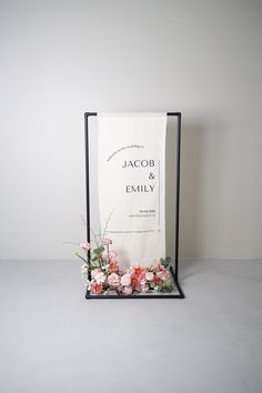 a sign with flowers on it sitting in front of a white wall next to a black frame