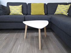 a gray couch sitting next to a white table on top of a hard wood floor