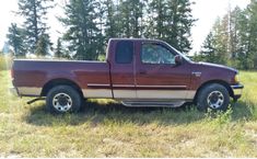 a red pick up truck parked in a field with trees behind it and grass on the ground