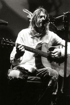 a man with long hair playing an acoustic guitar