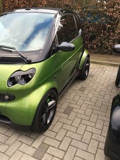 a green smart car parked on the side of a road next to another black car