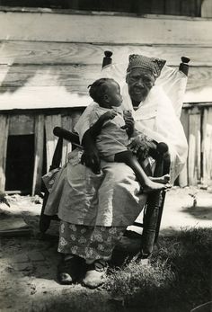 an old black and white photo of two women sitting on a chair holding a child