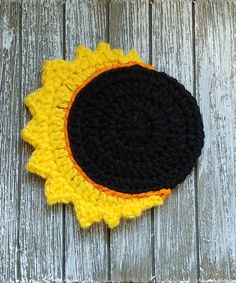 a crocheted black and yellow sunflower on a wooden table with white boards