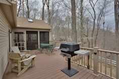 a grill on the back deck of a house with chairs and table in front of it