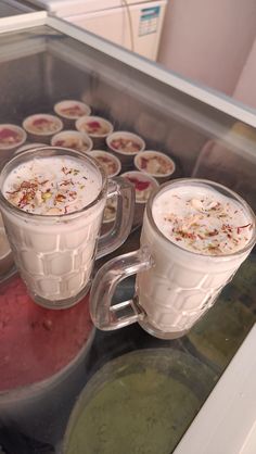 two mugs filled with liquid sitting on top of a counter next to other cups