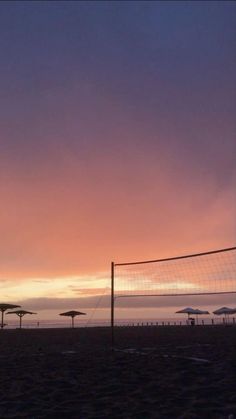 the sun is setting at the beach with umbrellas