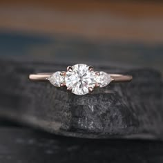 a three stone diamond ring sitting on top of a rock