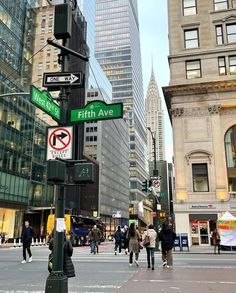 people are walking on the street in front of tall buildings with signs pointing to different streets