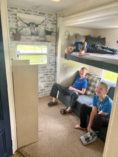 two boys are sitting on a couch in a small room with bunk beds and other furniture