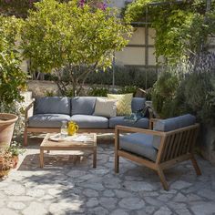 an outdoor seating area with blue couches and tables in the middle, surrounded by greenery