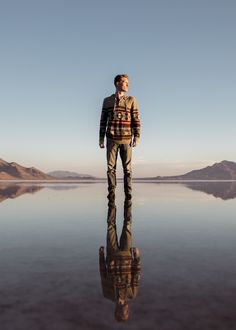 a man standing in front of a large body of water with mountains in the background