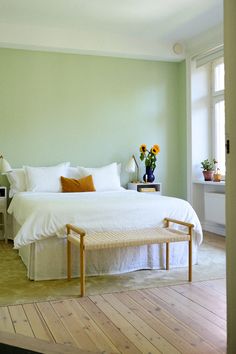 a white bed sitting in a bedroom next to a wooden table with two vases on top of it