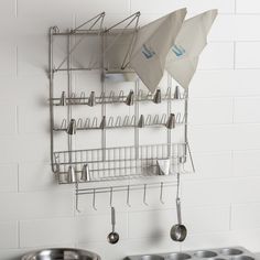 two pots and pans are hanging on the wall next to a rack with utensils