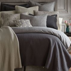 a bed covered in grey and black comforter next to a nightstand with flowers on it