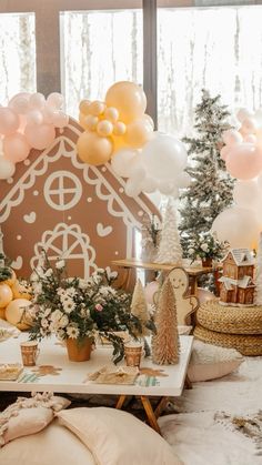 a table topped with lots of balloons next to a gingerbread house and christmas trees