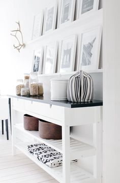 a white shelf with pictures and baskets on it in front of a wall filled with photos