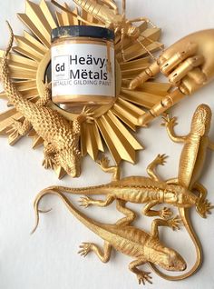 two gold lizards are next to a jar of heavy metal paint on a white surface