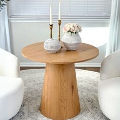 two white vases sitting on top of a wooden table in front of a window