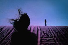 a person standing on top of a snow covered slope with their hair blowing in the wind