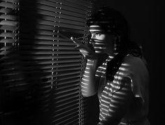 a woman standing next to a window with blinds covering her face and hand on the blind