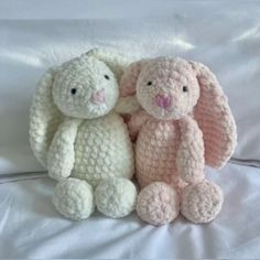 two crocheted stuffed animals sitting next to each other on a white bed sheet