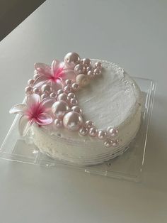 a white cake with pink flowers and pearls on it's top is in a plastic container