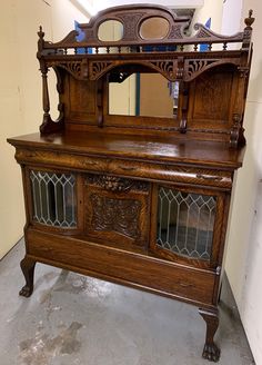 an old wooden cabinet with glass doors and carvings on the front door, in a room