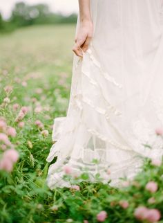 a woman in a white dress is walking through the grass with pink flowers on it