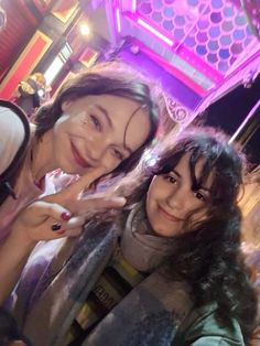 two women standing next to each other in front of a neon lit building at night