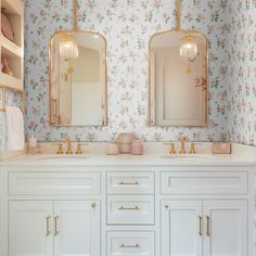 a bathroom with floral wallpaper and two mirrors above the sinks, gold faucets