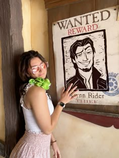 a young woman poses in front of a wanted reward sign with a bow tie around her neck