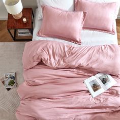 a bed with pink sheets and pillows on top of it next to a night stand