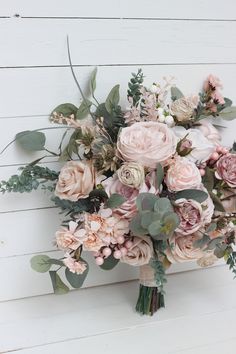 a bridal bouquet with pink flowers and greenery on a white wall in the background