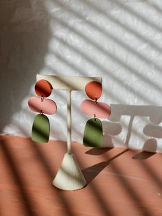 two pairs of earrings are hanging from a stand in front of a white wall with shadows on it