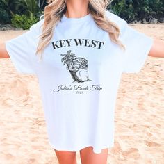 a woman on the beach wearing a key west t - shirt and sunglasses with her arms outstretched