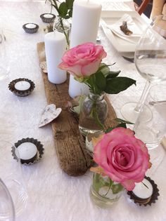 three pink roses in vases sitting on a table with empty wine glasses and candles