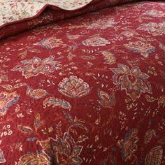 a bed with a red bedspread that has flowers on it and a white pillow