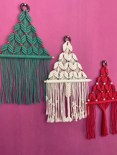 three different types of macrame hangings on a pink wall with red, green and white tassels