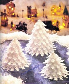 three snow covered trees in front of a christmas village with lights on the houses and buildings