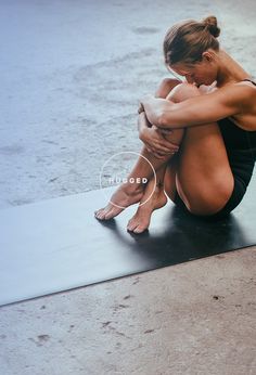 a woman sitting on top of a yoga mat with her arms folded over her knees