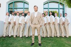 a man standing in front of a group of men wearing tan suits and ties with their hands in their pockets