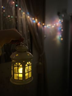 a person holding a lit lantern in front of a window with christmas lights on it