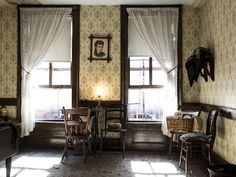 an old fashioned dining room with two windows and chairs in the corner, next to a piano