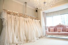 there are many wedding dresses hanging on the rack in front of a couch and chandelier