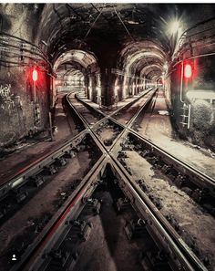 an underground train station with railroad tracks and red light at the end, in black and white